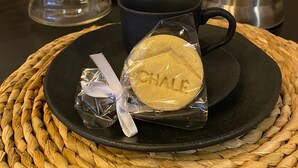 A coffee maker, a mug, and a cookie on a woven placemat.