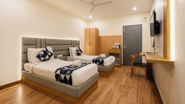 A hotel room with two beds, a desk, a chair, a wardrobe, a television, and a ceiling fan. - Whiteridge Premium (Hyderabad)