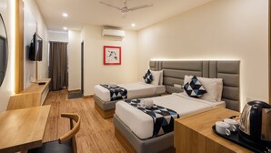 A hotel room with two beds, a desk, a chair, a TV, and a ceiling fan. - Whiteridge Premium (Hyderabad)