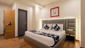 A modern hotel room with a large bed, a bedside table, a wardrobe, and a framed picture on the wall. - Whiteridge Premium (Hyderabad)