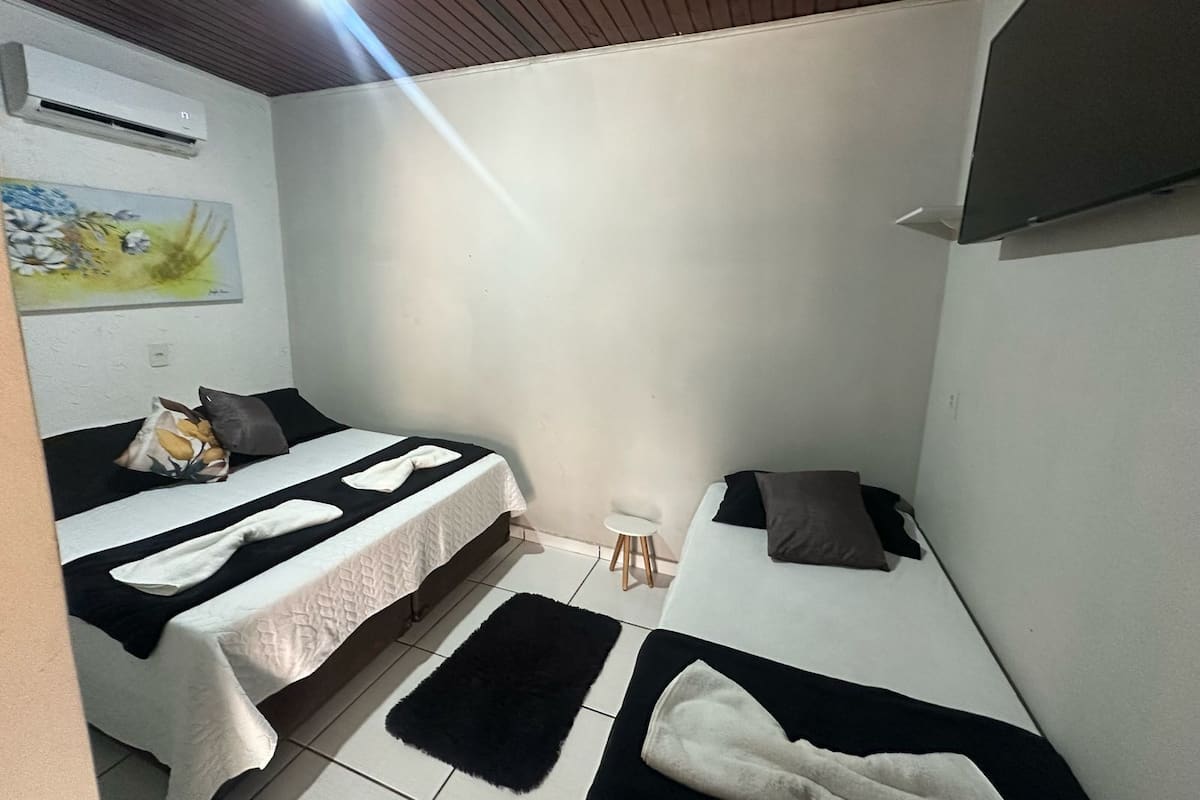 A small, compact room with two beds, a flat-screen TV mounted on the wall, and a small stool.