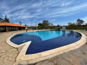 A swimming pool with a curved edge, surrounded by stone tiles and a covered seating area with a red roof. - PESQUE PAGUE JANGO (Cuiaba)