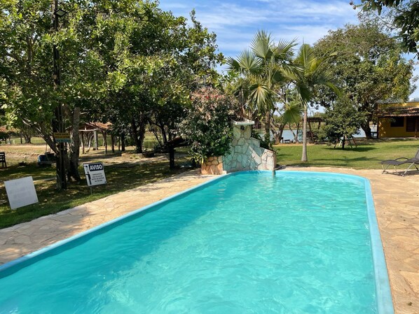 A swimming pool with clear blue water, surrounded by lush greenery and a stone wall. - PESQUE PAGUE JANGO (Cuiaba)