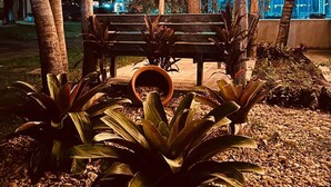 Una pérgola de madera con luces colgantes, un banco y plantas tropicales.