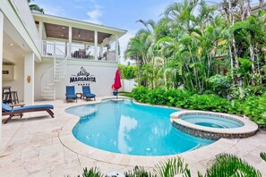 A pool area with lounge chairs, a covered seating area, and lush greenery. - Two Houses from Beach! Rooftop, Pool & Game Room (Holmes Beach)