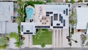 Luchtbeeld van een woonhuis met zwembad, terras met ligstoelen, een overdekte buitenkeuken en zonnepanelen.