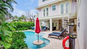 Área da piscina com espreguiçadeiras, um guarda-sol vermelho e um flutuador.