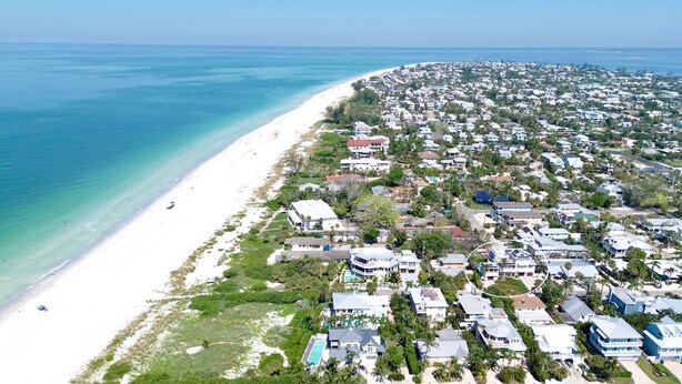 Vista aérea de uma área residencial costeira, com casas, praia e águas azul-claras.
