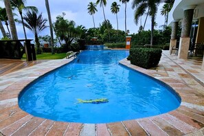 Une piscine à bord incurvé, entourée de palmiers et dotée d’une terrasse dallée.