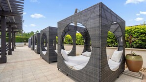 Des espaces de détente en plein air, avec des meubles en osier et des coussins blancs, disposés en rangées sur une terrasse carrelée.