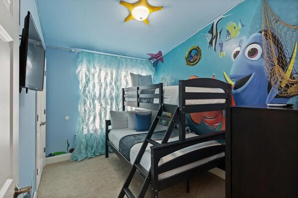Habitación infantil con literas, ventilador de techo y un mural de criaturas marinas animadas.