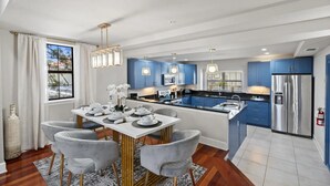 Une cuisine moderne avec des meubles bleus, un réfrigérateur en acier inoxydable et un coin repas comprenant une table blanche et des chaises grises.