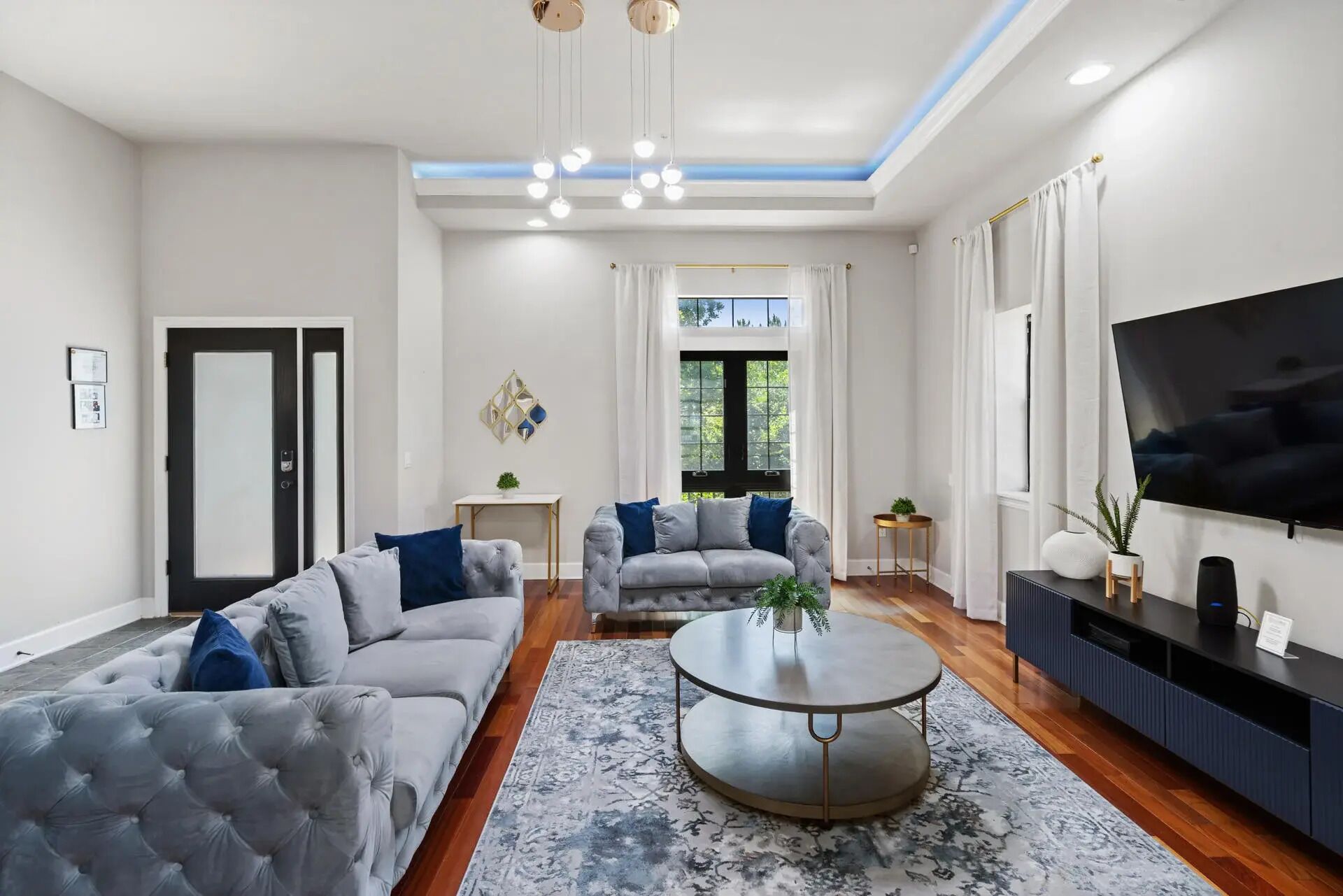 Un salon moderne avec un canapé gris, une table basse ronde et un téléviseur à écran plat fixé au mur.