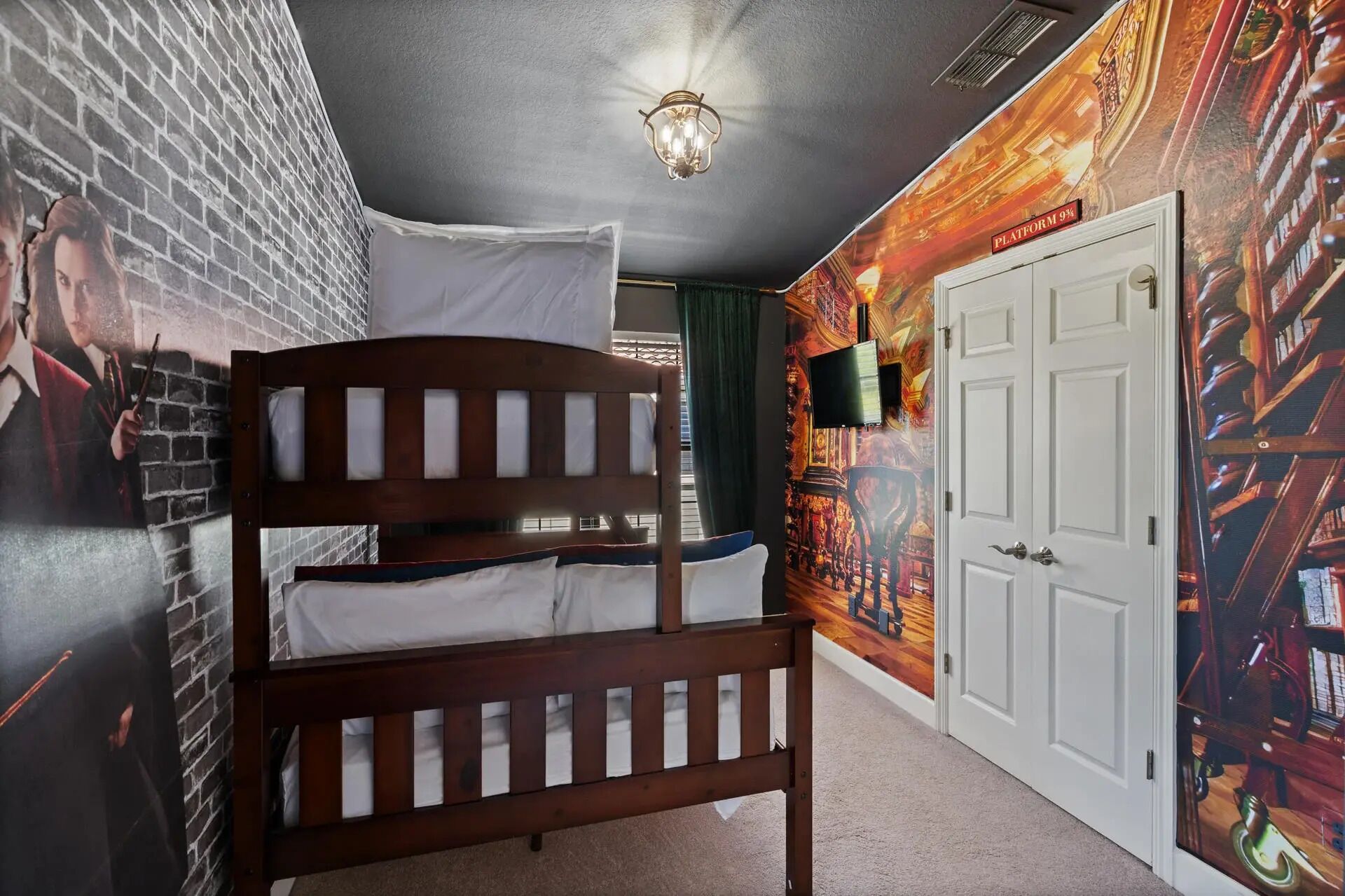 Een kamer met een stapelbed, een muurschildering van bakstenen, een plafondlamp en een deur met een platformbordje.