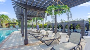 Un espace aménagé au bord de la piscine, avec des chaises longues, une pergola et des plantes suspendues.