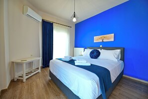 Una habitación de hotel con cama, mesita de noche, equipo de aire acondicionado y una pared azul de detalles.