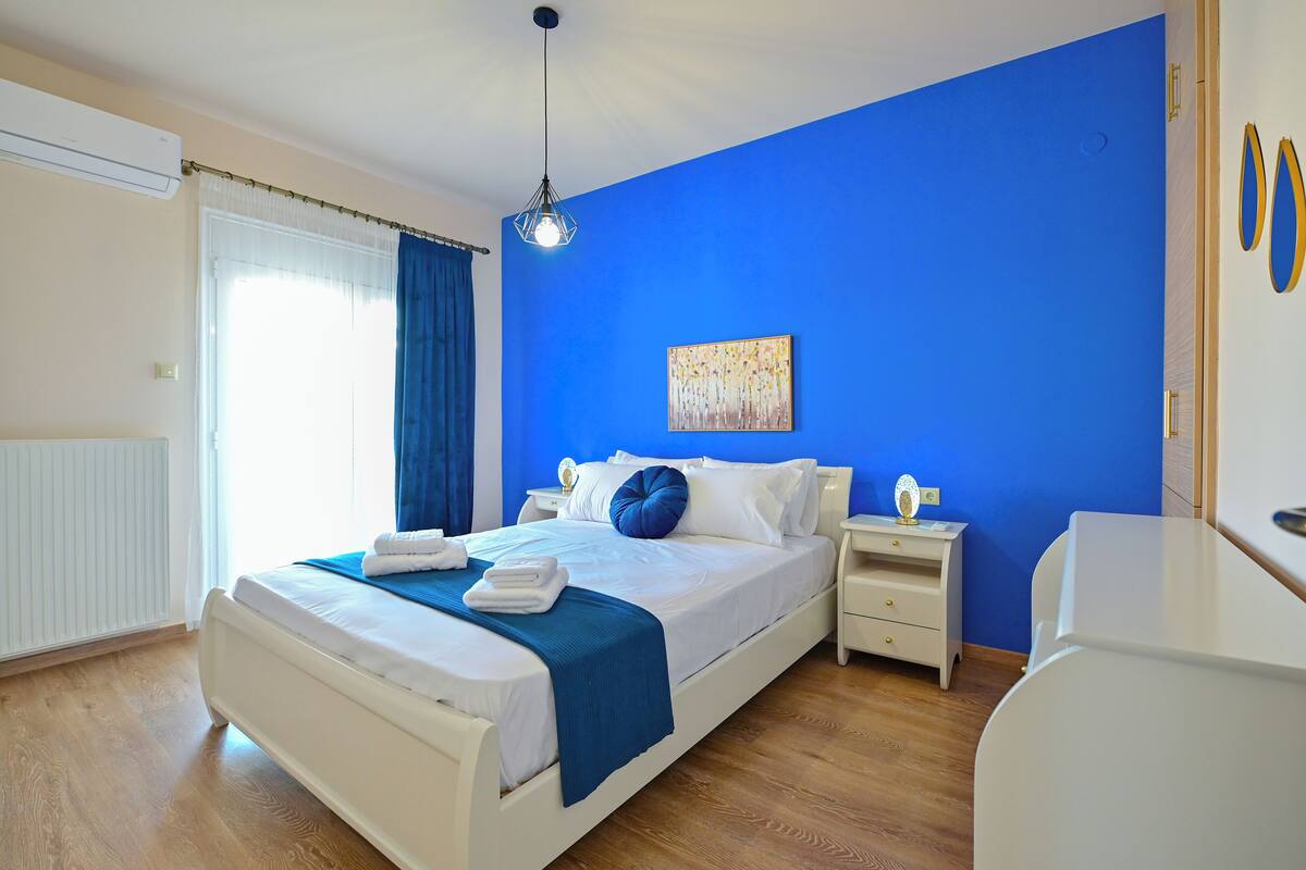 A bedroom with a large bed, white nightstands, a bedside table, and a blue accent wall.