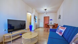 A modern living room with a flat-screen TV, a blue sofa, and a dining area with a table and chairs. - Royal Blue Central House by Checkin (Heraklion)