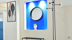 A hallway with a wooden floor, a black metal rack, a wall-mounted mirror, and framed artwork. - Royal Blue Central House by Checkin (Heraklion)
