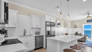 Une cuisine moderne avec des meubles blancs, des appareils en acier inoxydable et un îlot central doté de tabourets.