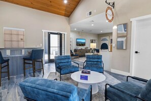 A spacious lobby with a reception desk, several seating areas with blue chairs, a round coffee table, and a large window offering a view of the outdoors.