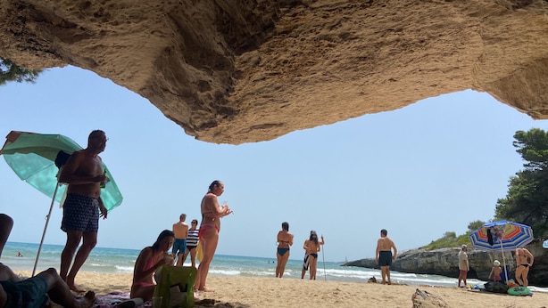 Een strandscène met mensen onder een rotsformatie.