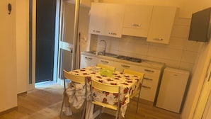Een kleine keuken met witte kastjes, een gasfornuis en een eettafel met een tafelkleed met bloemen.
