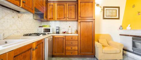 A kitchen with wooden cabinets, a microwave, a gas stove, and a chair near a fireplace.