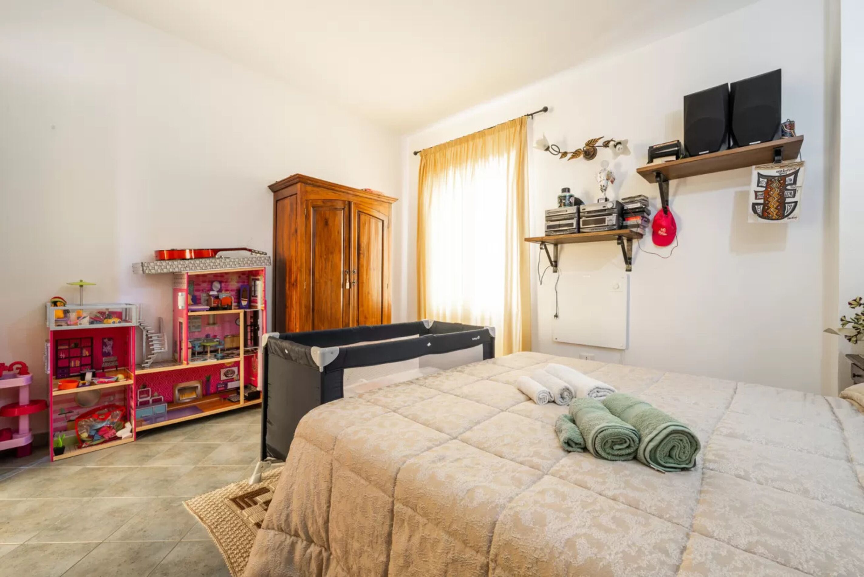Un dormitorio con una cama, un armario de madera, una estantería con altavoces y una casa de muñecas.