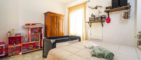 Un dormitorio con una cama, un armario de madera, una estantería con altavoces y una casa de muñecas.