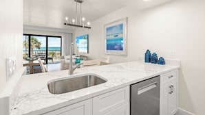 A modern kitchen with a large sink, white cabinets, and a view of the ocean through large windows. - Direct Beachfront and View | Walk-Out to Sand | Pool + Pickleball + Tennis | (Captiva)