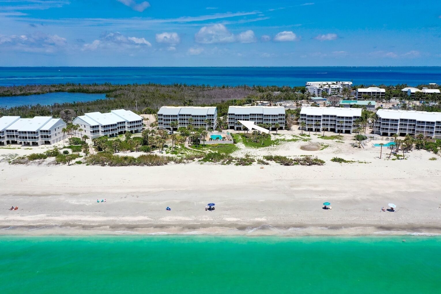 A beachfront hotel with multiple buildings, a sandy beach, and clear turquoise waters.