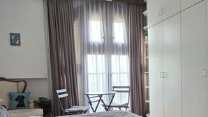 A bedroom with a large bed, a chandelier, a wardrobe, and a window with curtains.
