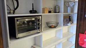 A kitchen with white shelves, a coffee maker, a kettle, a toaster, and a trash can.