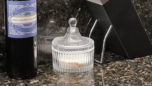 A bottle of wine, a glass container, and a knife block on a granite countertop.