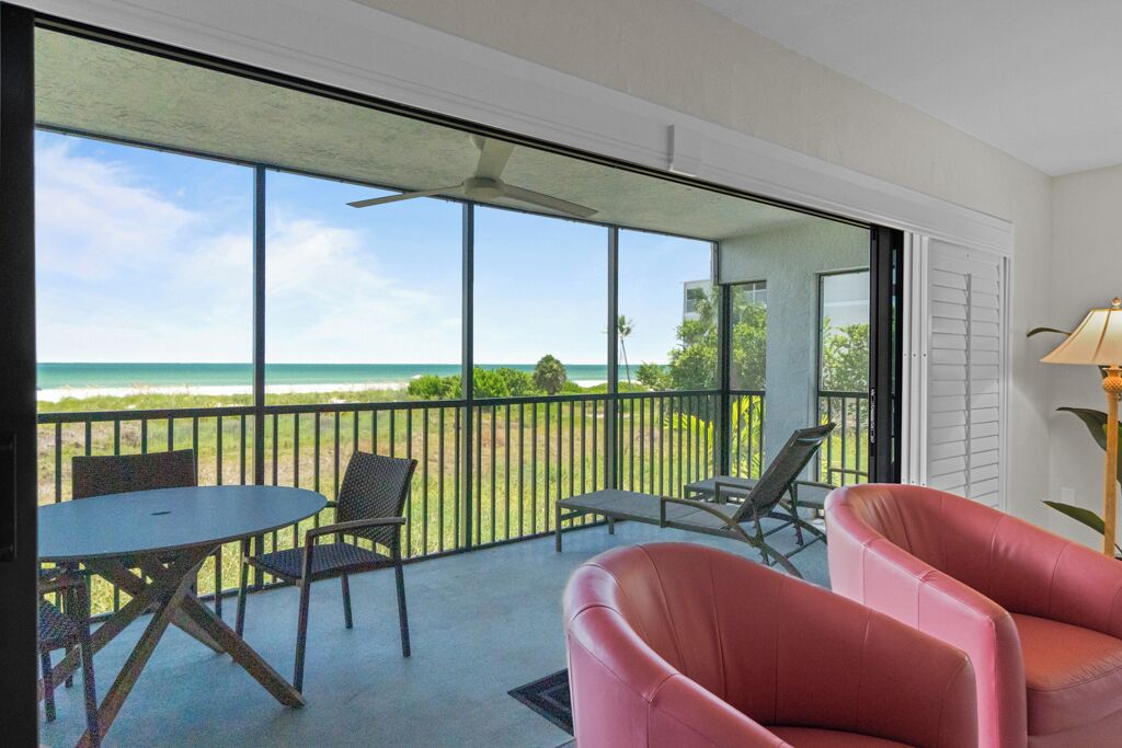 A balcony with a view of the ocean, a table with chairs, and a pink chair.