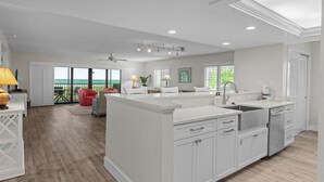A spacious kitchen with a large island, white cabinetry, and a view of the ocean through large windows.