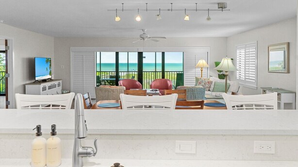 A modern living room with a view of the ocean, white furniture, and a ceiling fan.
