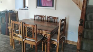 Un comedor con una mesa y sillas de madera, un cuadro en la pared y una escalera.