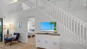 Ein modernes Wohnzimmer mit Treppe, einem Flachbildfernseher und Blick auf den Strand.