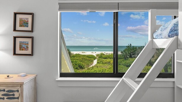Ein Schlafzimmer mit großem Fenster und Blick auf einen Strand, ein Bett und eine Kommode mit Fischornamenten.