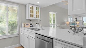 A modern kitchen with white cabinetry, a stainless steel dishwasher, and a large island with a sink. - Sun, Serenity & Space: Perfect Family Escape at Seagrape Village on Sanibel (Sanibel)