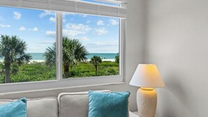 A room with a view of the beach, a white lamp, and a beige sofa with blue cushions. - Sun, Serenity & Space: Perfect Family Escape at Seagrape Village on Sanibel (Sanibel)