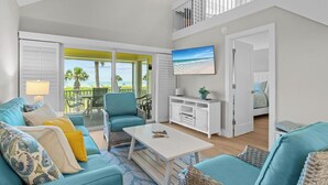 A spacious living area with a balcony, a white coffee table, and a television mounted on the wall. - Sun, Serenity & Space: Perfect Family Escape at Seagrape Village on Sanibel (Sanibel)