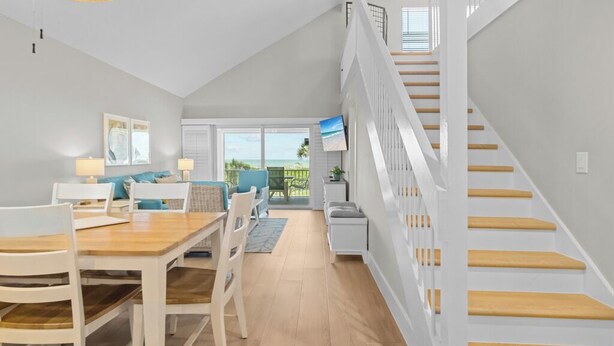A spacious living area with a wooden dining table, white chairs, a sofa, and a staircase with wooden steps. - Sun, Serenity & Space: Perfect Family Escape at Seagrape Village on Sanibel (Sanibel)