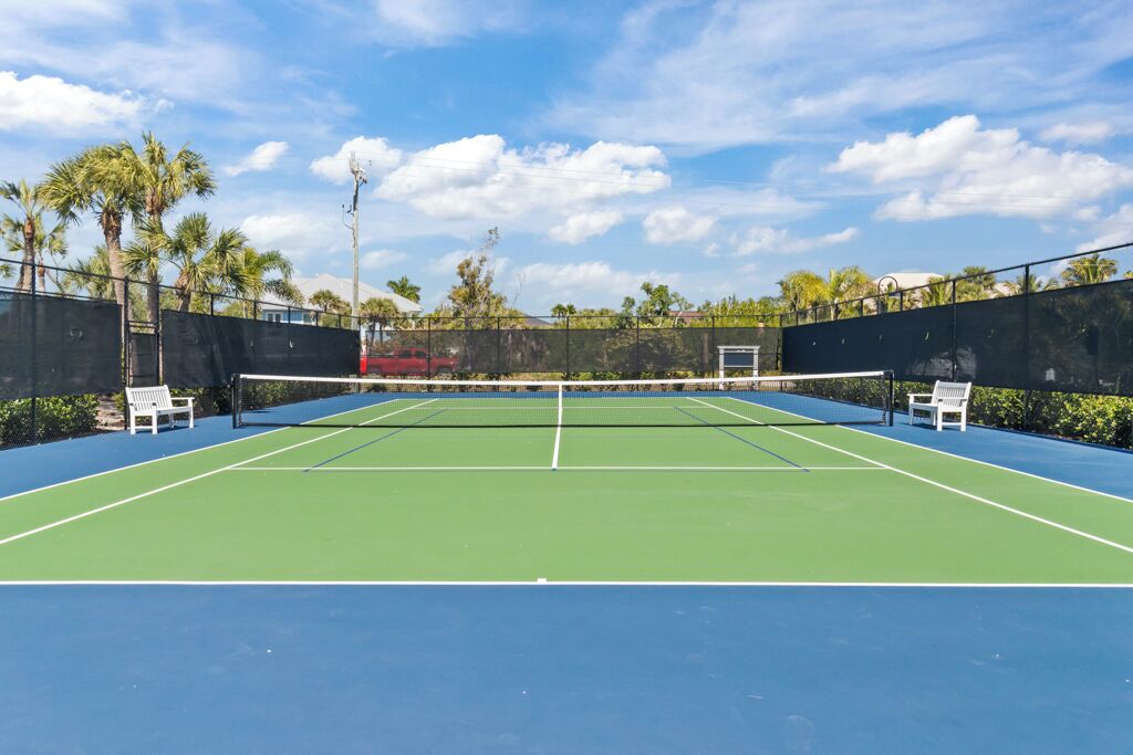 Een tennisbaan buiten, met een net, omheind door een hek en voorzien van bankjes.