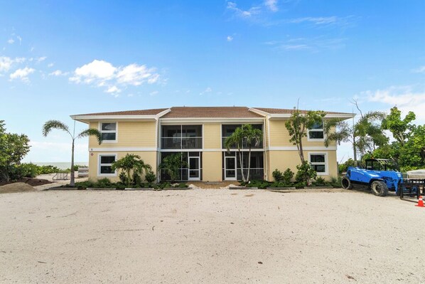 A two-story building with a flat roof, large windows, and a sandy ground area in front.