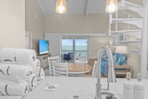 A hotel room with a balcony, a round dining table, white furniture, and a TV.