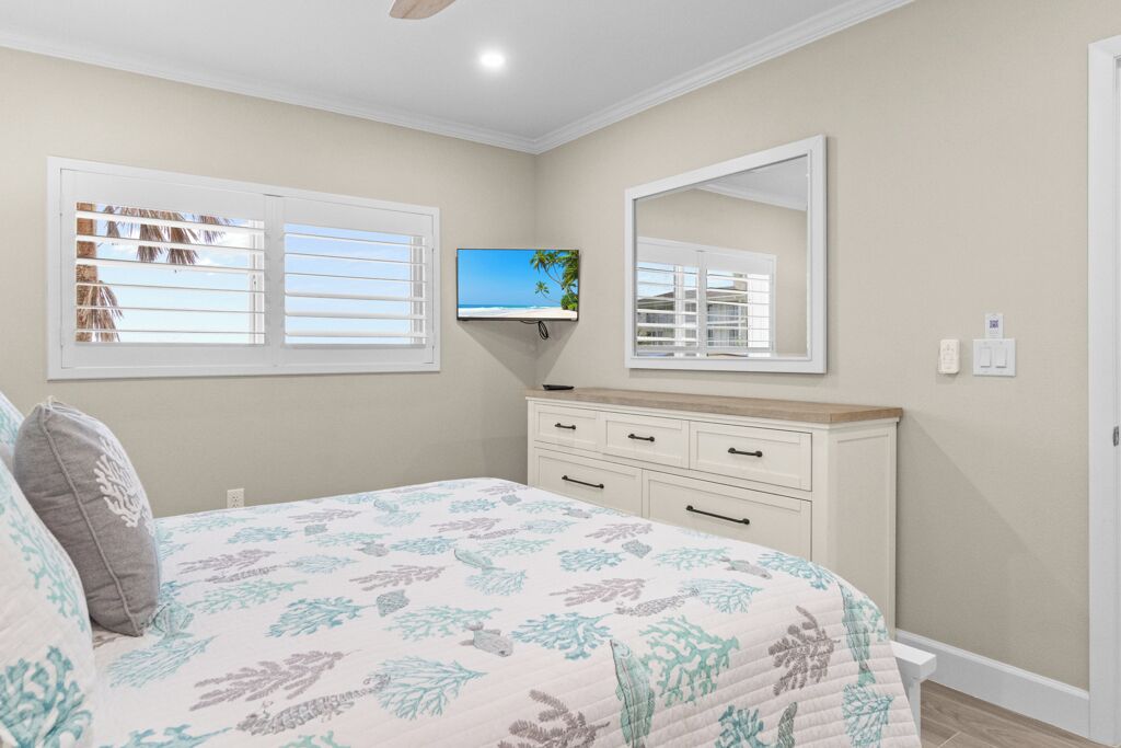 A bedroom with a bed, a TV mounted on the wall, a dresser, and a window with blinds.