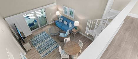 A spacious living area with a blue sofa, round coffee table, and white chairs. There is a large window with blinds, a ceiling fan, and a staircase leading to another level.